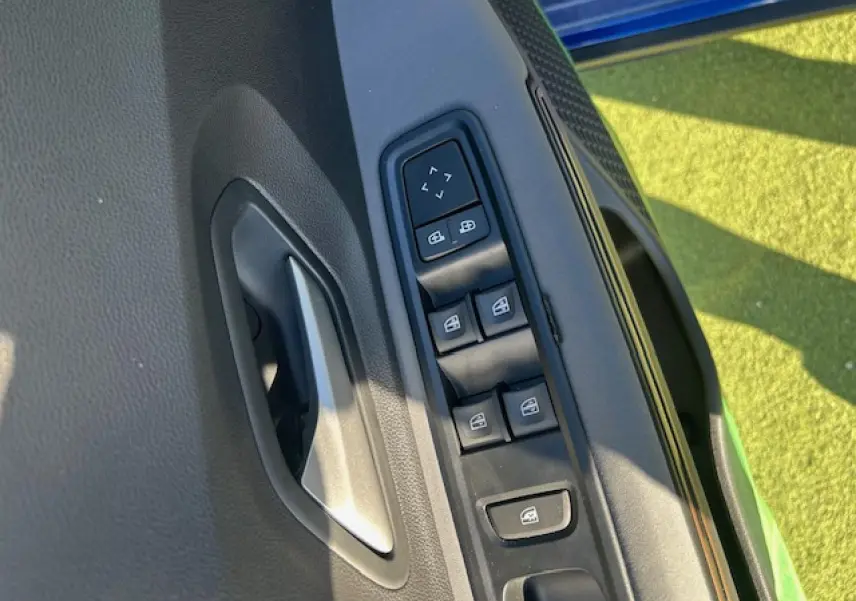 Détail des commandes de lève-vitres et rétroviseurs sur la porte côté gauche d’une Dacia Sandero III Stepway bleu Iron.