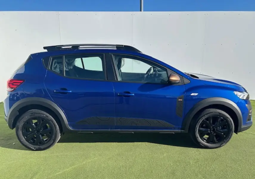 Profil côté gauche d'une Dacia Sandero Stepway bleu iron avec jantes noires et barres de toit grises sur fond clair.