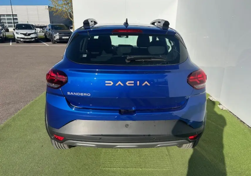 Vue arrière d'une Dacia Sandero III Stepway bleu Iron avec barres de toit et logo Dacia brun cuivré.