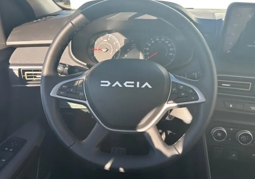 Vue centrée sur le volant noir du Dacia Sandero 2025 avec tableau de bord et commandes visibles en arrière-plan.