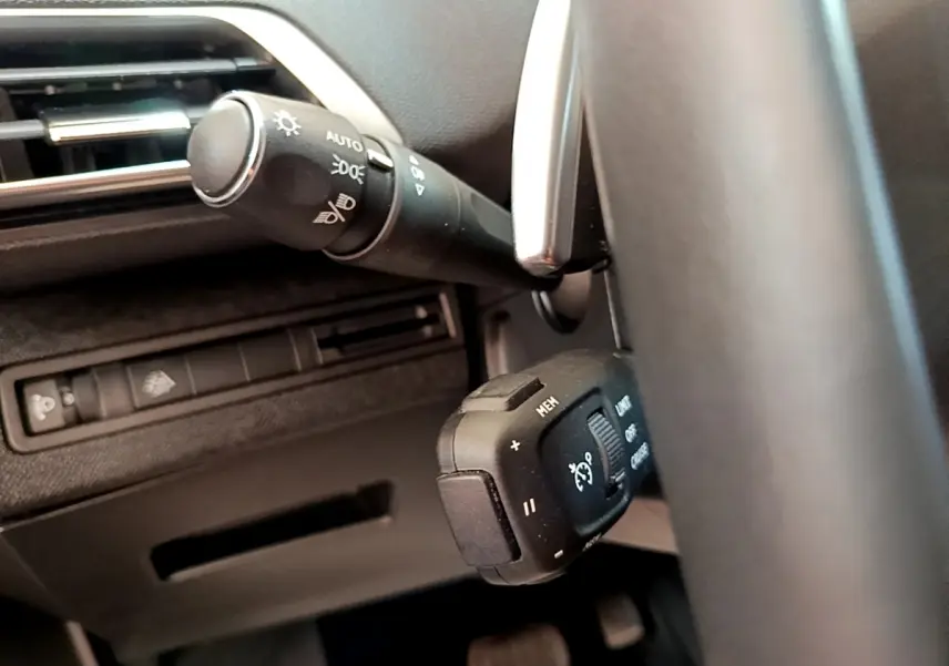Gros plan sur la commande de régulateur de vitesse et éclairage côté gauche du volant d’un Peugeot 3008 gris foncé 2022.