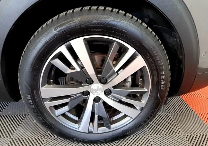 Gros plan sur la roue avant droite d’un Peugeot 3008 gris foncé, jante alliage à cinq branches doubles.