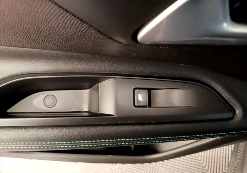 Gros plan sur la commande de lève-vitre côté gauche du Peugeot 3008 gris foncé, avec surpiqûres bleues visibles.