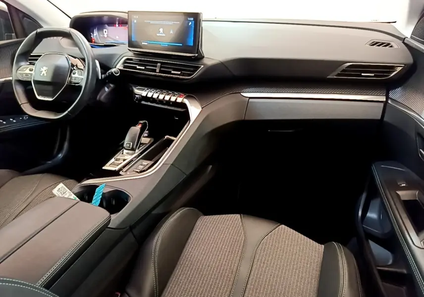 Vue intérieure côté passager du tableau de bord et console centrale du Peugeot 3008 gris foncé avec écran tactile et volant cuir.