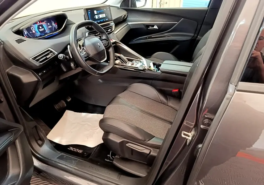Vue intérieure côté conducteur du Peugeot 3008 gris foncé, avec tableau de bord digital et sièges en tissu et cuir.