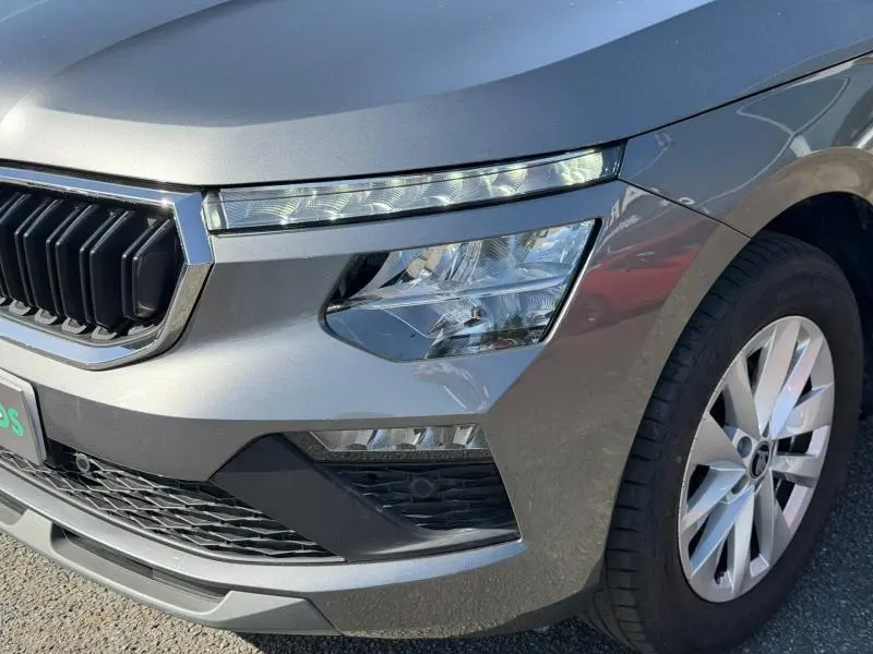 Gros plan sur l'avant droit du Skoda Kamiq gris graphite métallisé, mettant en valeur le phare et la calandre distinctive.