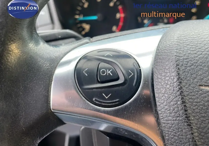 Gros plan sur les commandes au volant noir et argent du Ford Transit Custom blanc, modèle 2016, avec tableau de bord flou en arrière-plan.