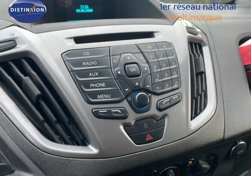 Vue rapprochée de la console centrale grise du Ford Transit Custom blanc, avec commandes radio et climatisation visibles.