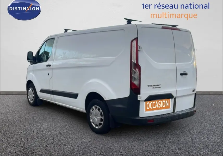 Ford Transit Custom blanc vu en 3/4 arrière côté gauche avec porte arrière et plaque occasion visible.