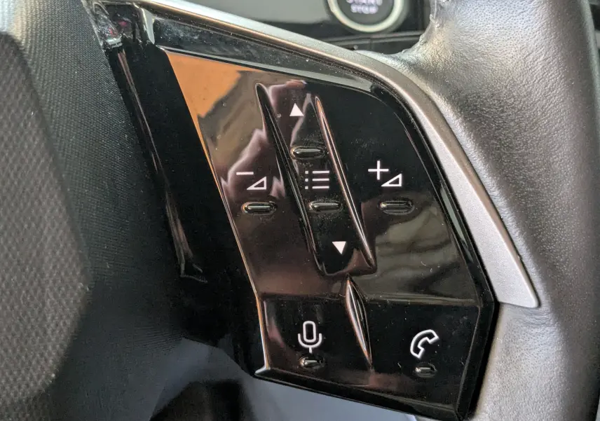 Gros plan sur les commandes noires du volant cuir du Peugeot 3008 Hybrid 145 eDCS6 Allure blanc, avec boutons de volume et téléphone.