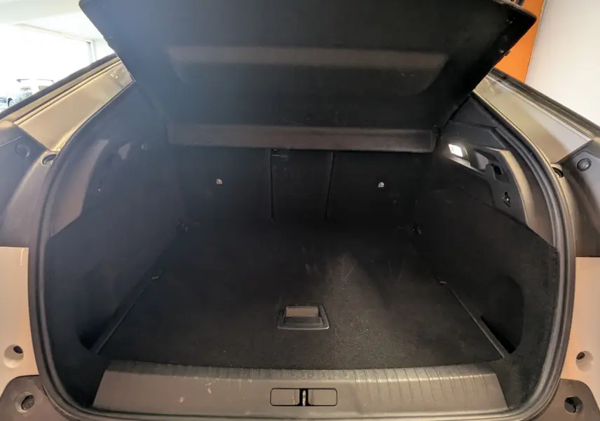 Coffre ouvert du Peugeot 3008 Hybrid blanc, vue arrière montrant l’espace de chargement noir et l’éclairage intérieur.