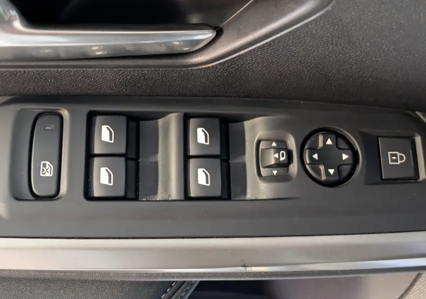 Vue rapprochée des commandes de lève-vitres et réglages des rétroviseurs sur la porte côté conducteur d’un Peugeot 3008 blanc.