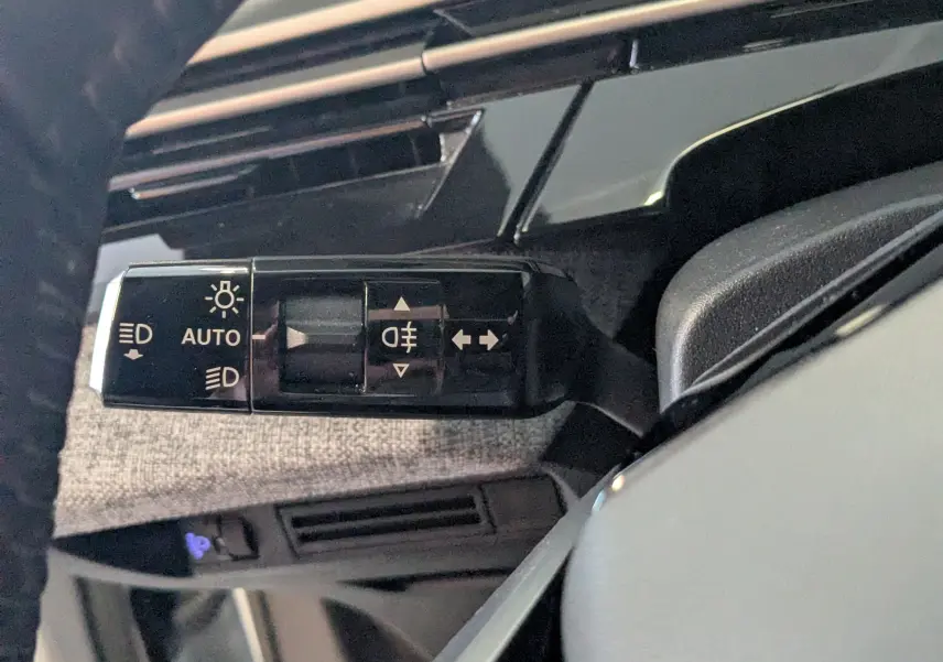 Gros plan sur la commande des feux à gauche du volant dans l’habitacle gris clair du Peugeot 3008 Hybrid blanc.