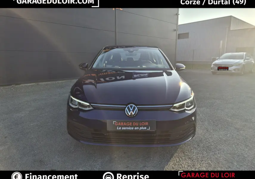 Vue avant d'une Volkswagen Golf bleu foncé 2023 avec phares LED et logo VW bien visible sur un parking extérieur.