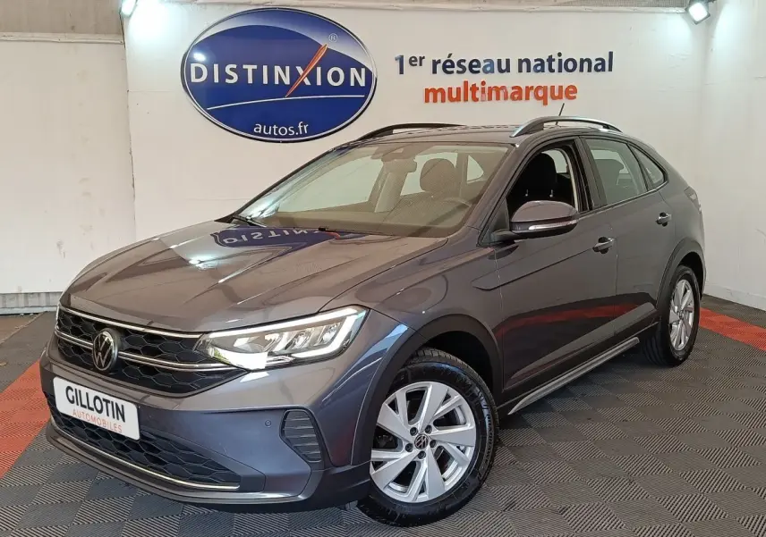 Volkswagen Taigo gris foncé en 3/4 avant droit dans un showroom avec logo Distinxion en arrière-plan.