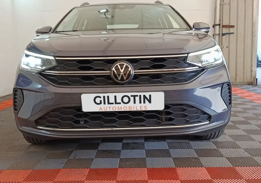 Vue frontale d'un Volkswagen Taigo gris foncé avec phares allumés et calandre hexagonale distinctive.