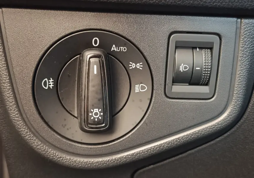 Gros plan sur la molette de réglage des phares et le bouton de réglage en hauteur dans un Volkswagen Taigo gris foncé.