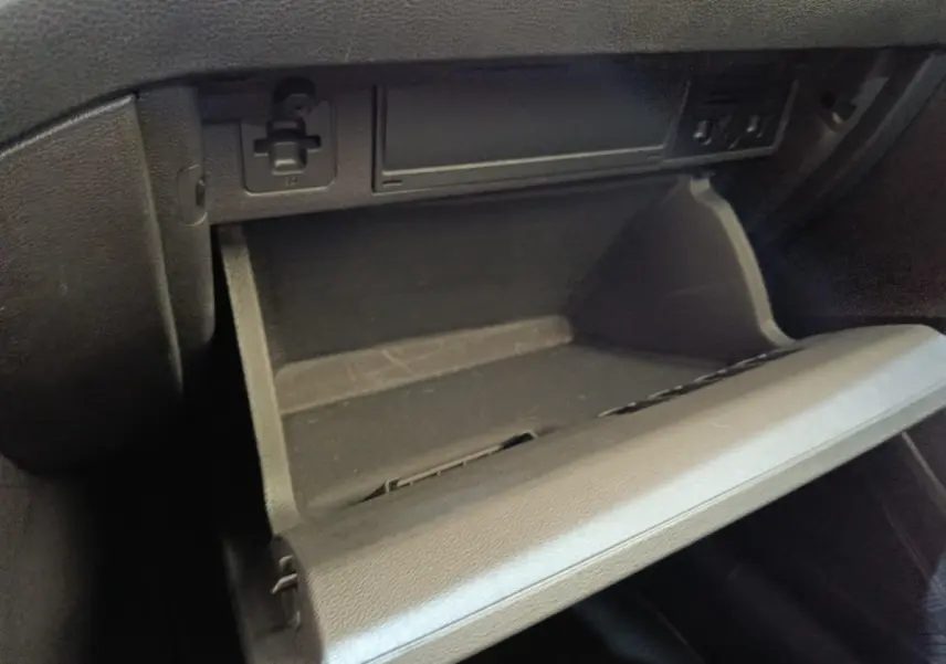 Gros plan sur la boîte à gants ouverte côté passager du Volkswagen Taigo gris foncé, intérieur noir.