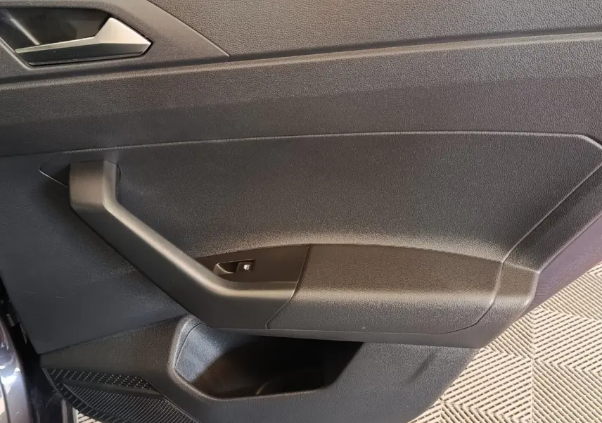 Gros plan sur la porte intérieure côté gauche du Volkswagen Taigo gris foncé, montrant la poignée et le bouton de lève-vitre.