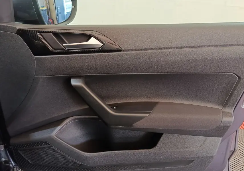 Vue rapprochée de la porte côté conducteur du Volkswagen Taigo gris foncé, avec poignée et panneau de commande des vitres.