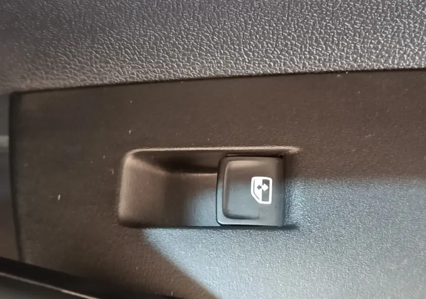 Gros plan sur le bouton de commande de lève-vitre arrière droit dans l'habitacle d'un Volkswagen Taigo gris foncé.