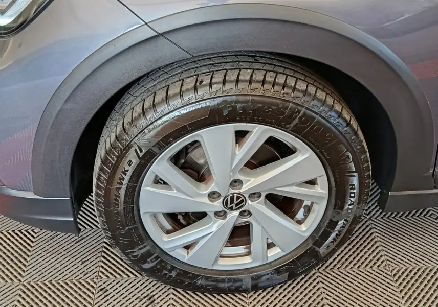 Gros plan sur la roue avant gauche d’un Volkswagen Taigo gris foncé, mettant en valeur la jante et le pneu Firestone.