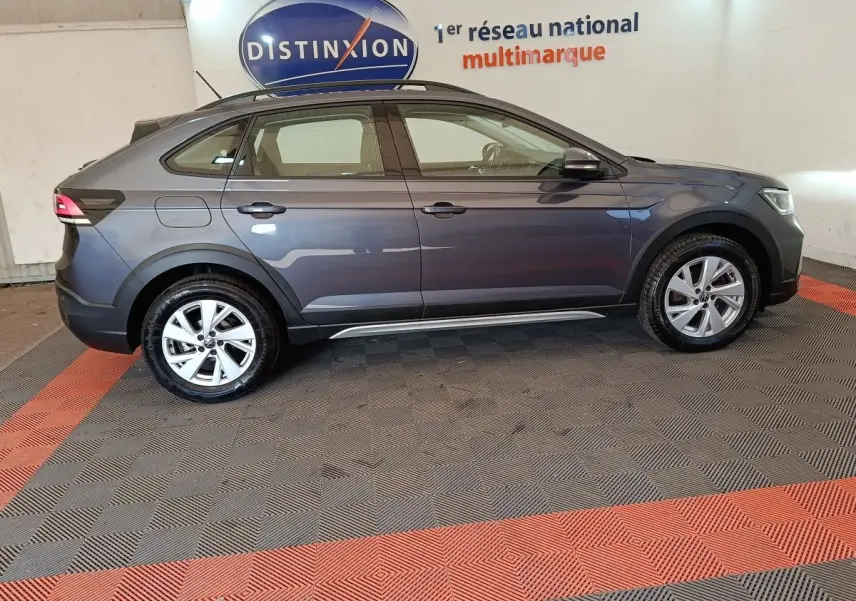 Vue de profil côté gauche d’un Volkswagen Taigo gris foncé 2023 garé en intérieur sur sol à damiers rouges et gris.