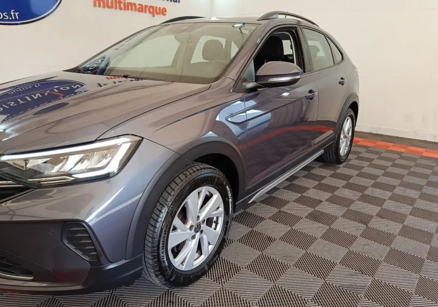 Vue 3/4 avant droit d’un Volkswagen Taigo gris foncé, mettant en valeur ses phares LED et jantes alliage.