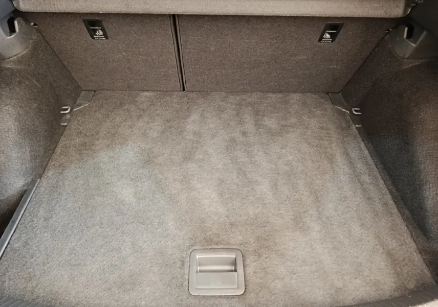 Coffre spacieux et vide du Volkswagen Taigo gris foncé, avec revêtement en tissu et poignées de fixation visibles.