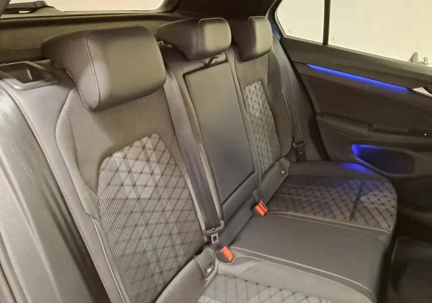Vue intérieure des sièges arrière de la Volkswagen Golf 1.5 eTSI, avec éclairage d'ambiance bleu sur la porte.