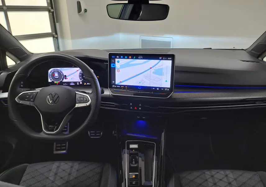 Vue intérieure du poste de conduite de la Volkswagen Golf 1.5 eTSI R-Line 2025 avec écran tactile et éclairage d'ambiance bleu.