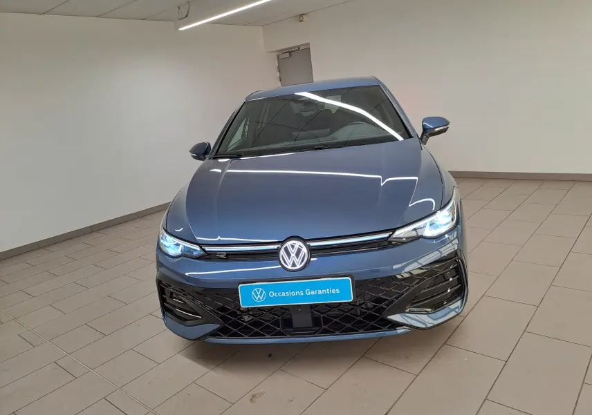 Vue avant d'une Volkswagen Golf 1.5 eTSI R-Line bleu anémone avec phares allumés dans un showroom.