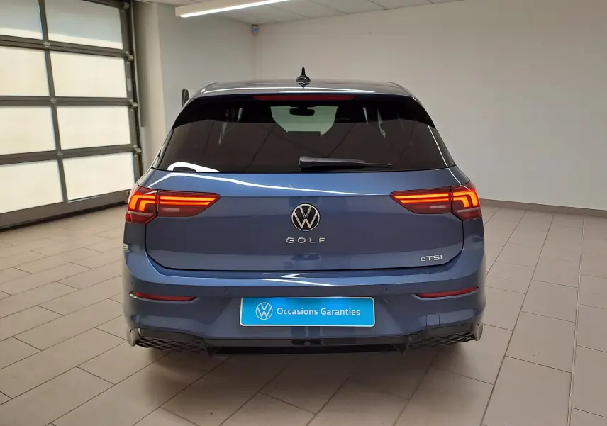 Vue arrière d'une Volkswagen Golf 1.5 eTSI 150 DSG7 R-Line Edition bleu Anémone avec feux allumés en intérieur.