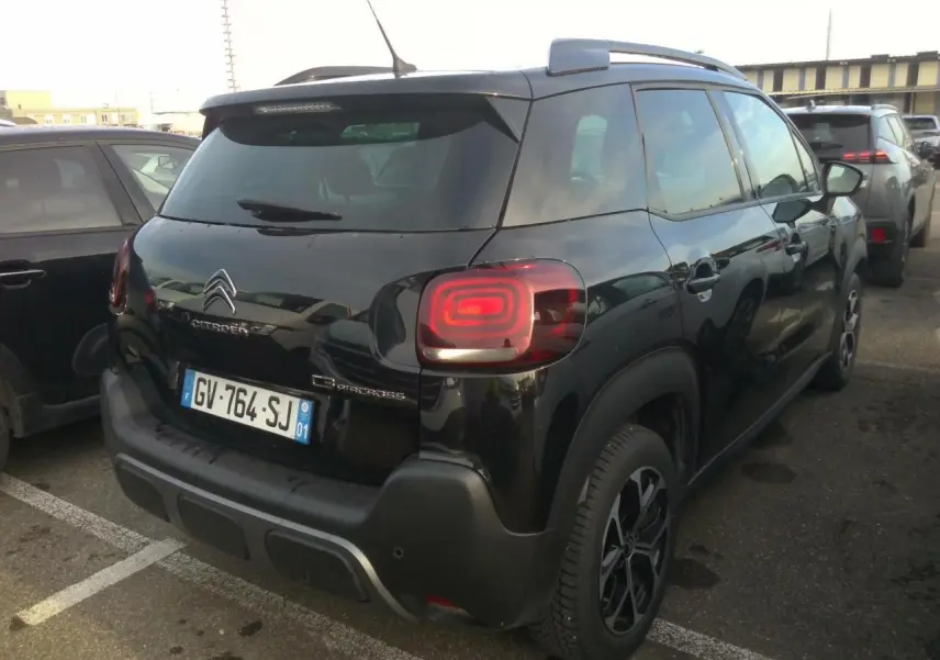 Vue 3/4 arrière droite d'un Citroën C3 Aircross noir avec jantes alliage diamantées et barres de toit noires.