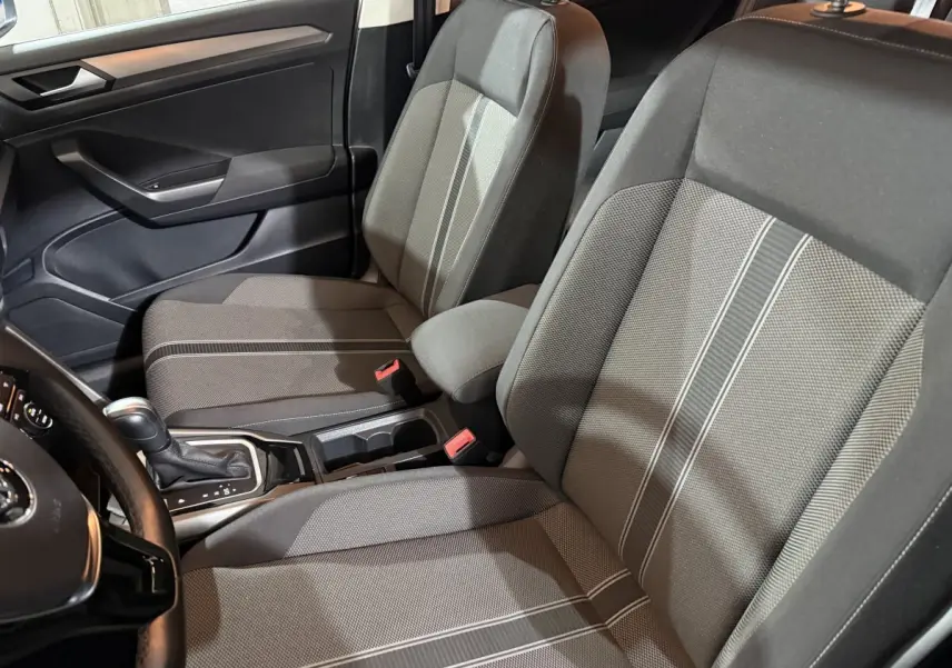 Vue intérieure côté conducteur du Volkswagen T-Roc 1.5 TSI blanc, sièges tissu gris avec bandes claires et console centrale visible.