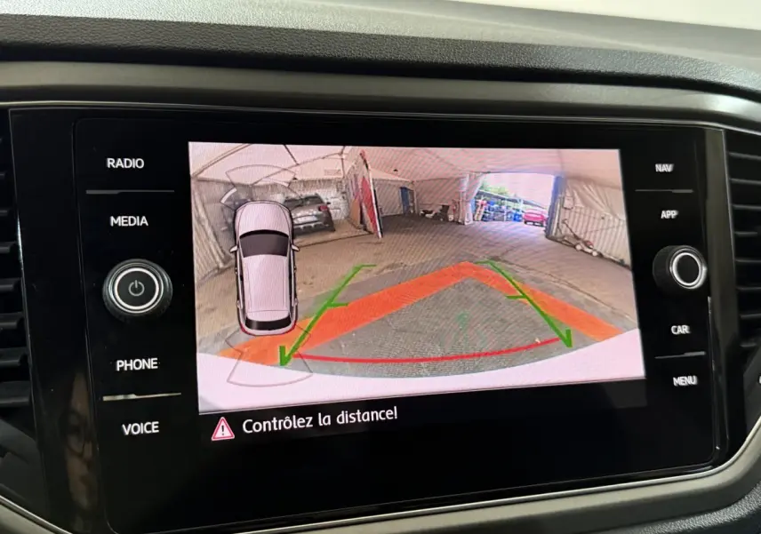 Écran tactile du tableau de bord affichant la caméra de recul du Volkswagen T-Roc blanc en intérieur de garage.