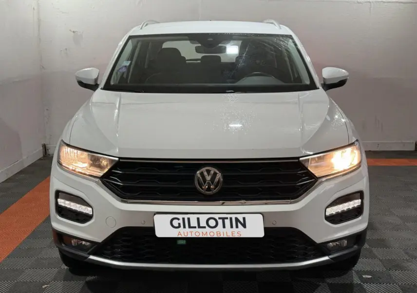 Volkswagen T-Roc blanc vue de face avec phares allumés et calandre noire dans un garage.