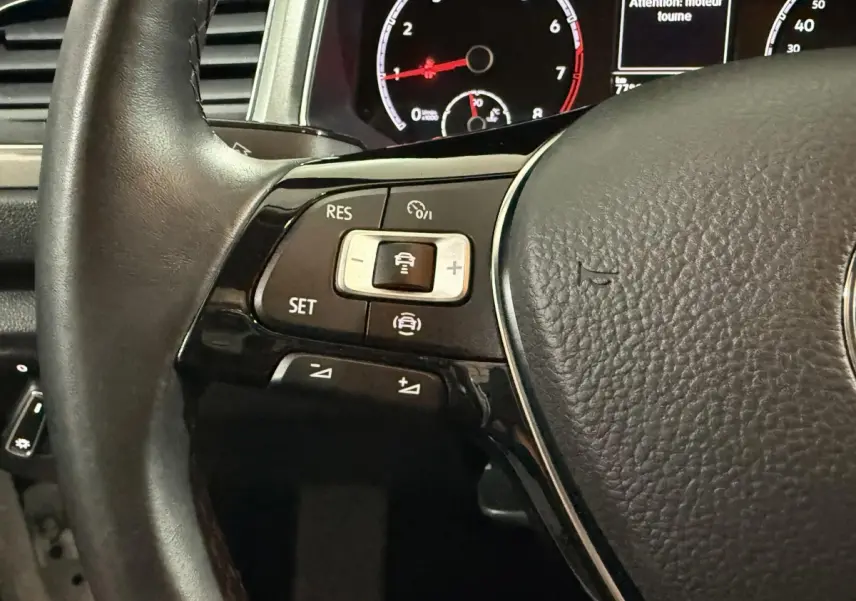 Gros plan sur le volant cuir noir du Volkswagen T-Roc 2020, avec commandes de régulateur adaptatif et tableau de bord numérique visible.