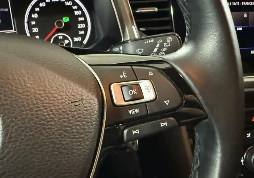 Gros plan sur le volant cuir noir du Volkswagen T-Roc 2020, avec commandes multifonctions et tableau de bord partiellement visible.