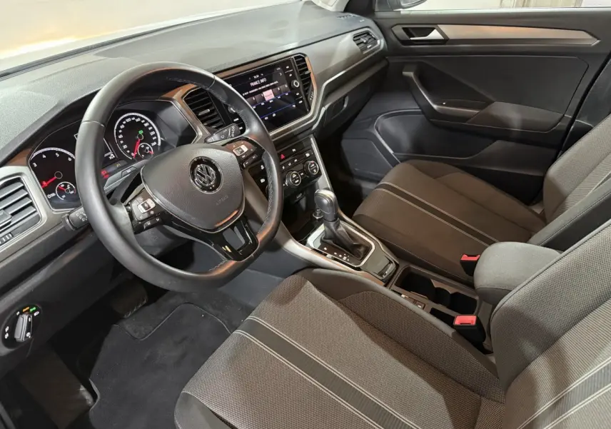 Intérieur du Volkswagen T-Roc 2020 vu côté conducteur, volant cuir noir et console centrale avec écran tactile.