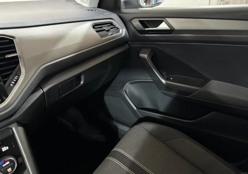 Intérieur côté passager du Volkswagen T-Roc blanc 2020, montrant la porte, tableau de bord et siège tissu gris.