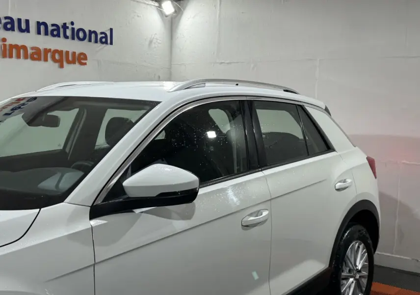 Vue côté gauche du Volkswagen T-Roc blanc 2020 en intérieur, mettant en valeur les rétroviseurs et les jantes alliage.