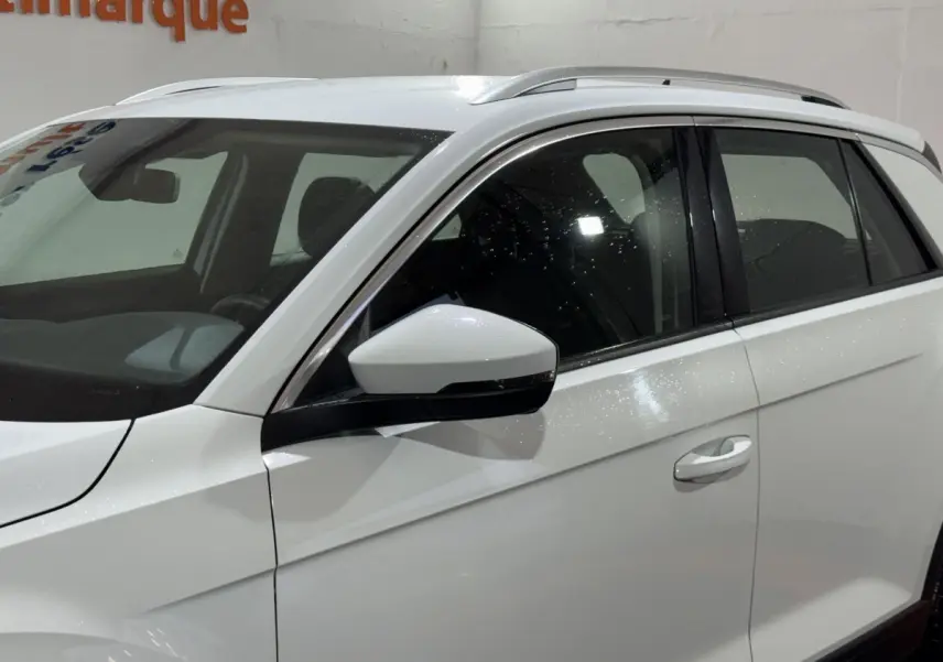 Vue latérale côté gauche d'un Volkswagen T-Roc blanc avec rétroviseurs électriques et rails de toit noirs.