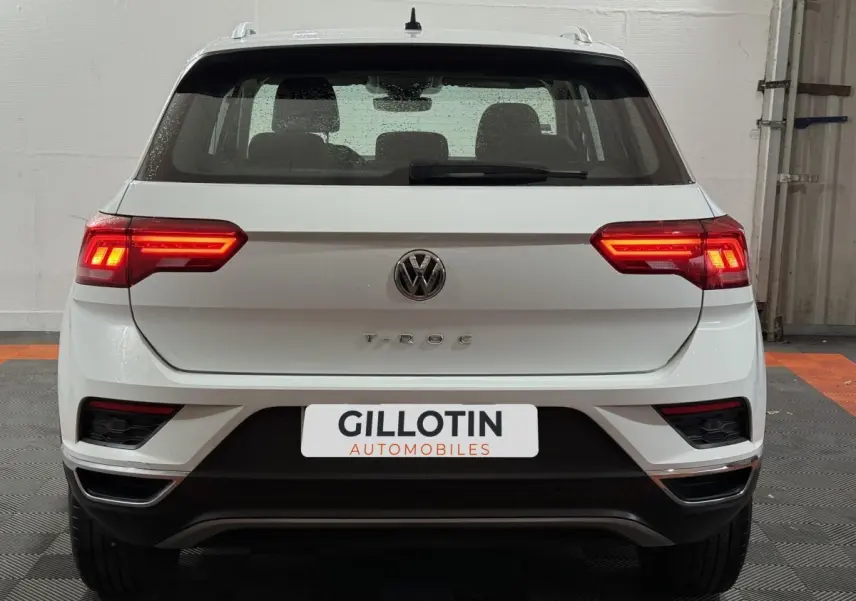 Vue arrière d'un Volkswagen T-Roc blanc 2020 avec feux LED allumés et logo visible sur un fond intérieur neutre.