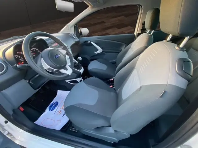 Vue intérieure côté conducteur de la Ford KA 1.2 69 Trend blanche de 2015, montrant les sièges et le volant.