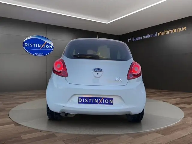 Vue arrière d'une Ford Ka blanche 2015 dans un showroom, avec feux rouges et logo visible sur le hayon.