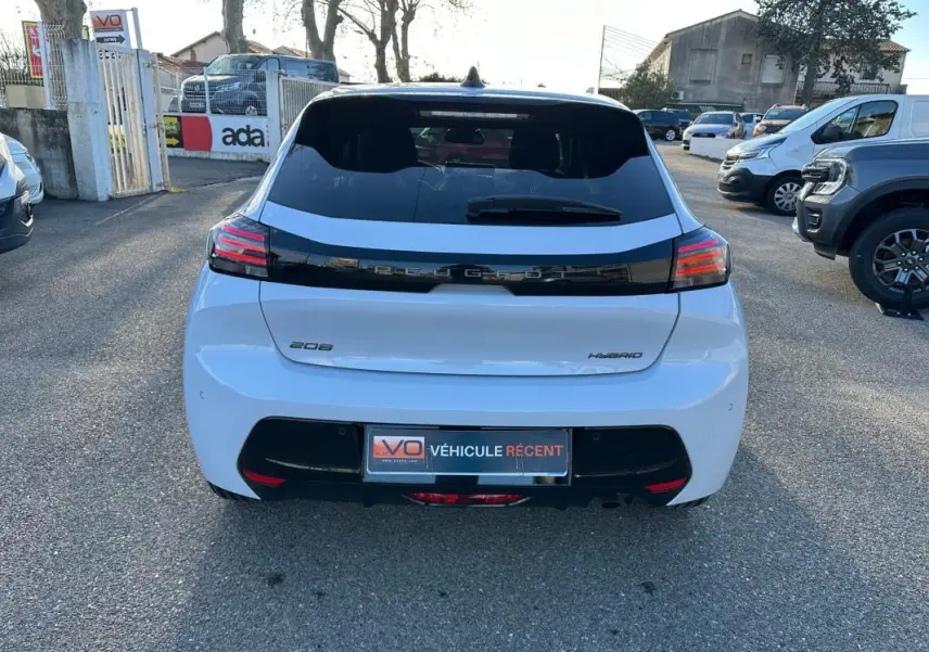 Vue arrière d'une Peugeot 208 Hybrid blanche de 2025 avec feux arrière LED et bande noire distinctive sur le hayon.