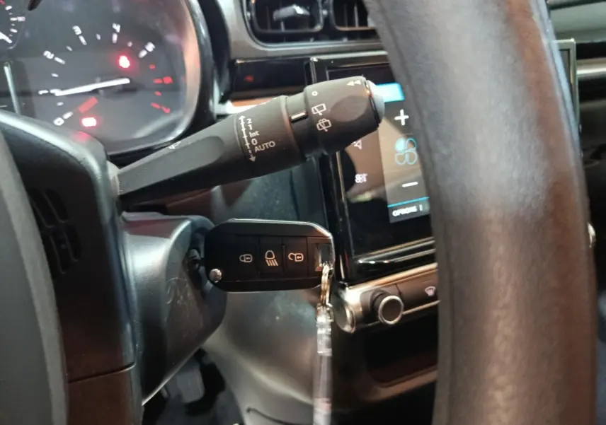 Gros plan sur le volant et la clé de contact d'une Citroën C3 gris foncé, avec tableau de bord tactile en arrière-plan.