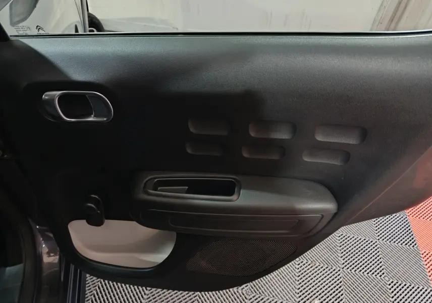 Vue intérieure de la porte côté conducteur de la Citroën C3 gris foncé, avec poignée intégrée et motifs rectangulaires.