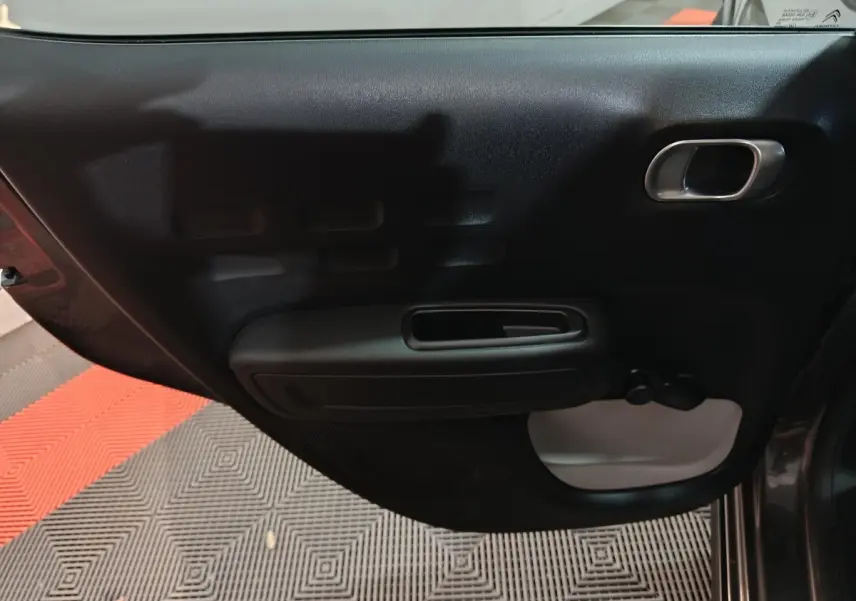 Vue intérieure de la porte arrière droite d'une Citroën C3 gris foncé, avec poignée et manivelle de vitre.